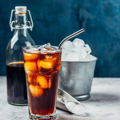 Glass of cold brew iced coffee made with Blade & Bean Black Label Six-Shooter with a bottle and ice cubes on a marble surface