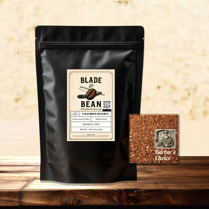 A black stand-up coffee pouch labeled Blade & Bean Cold Brew Reserve stands on a wooden surface against a textured beige wall, with a small square of the coarse ground coffee labeled Barber's Choice beside it.