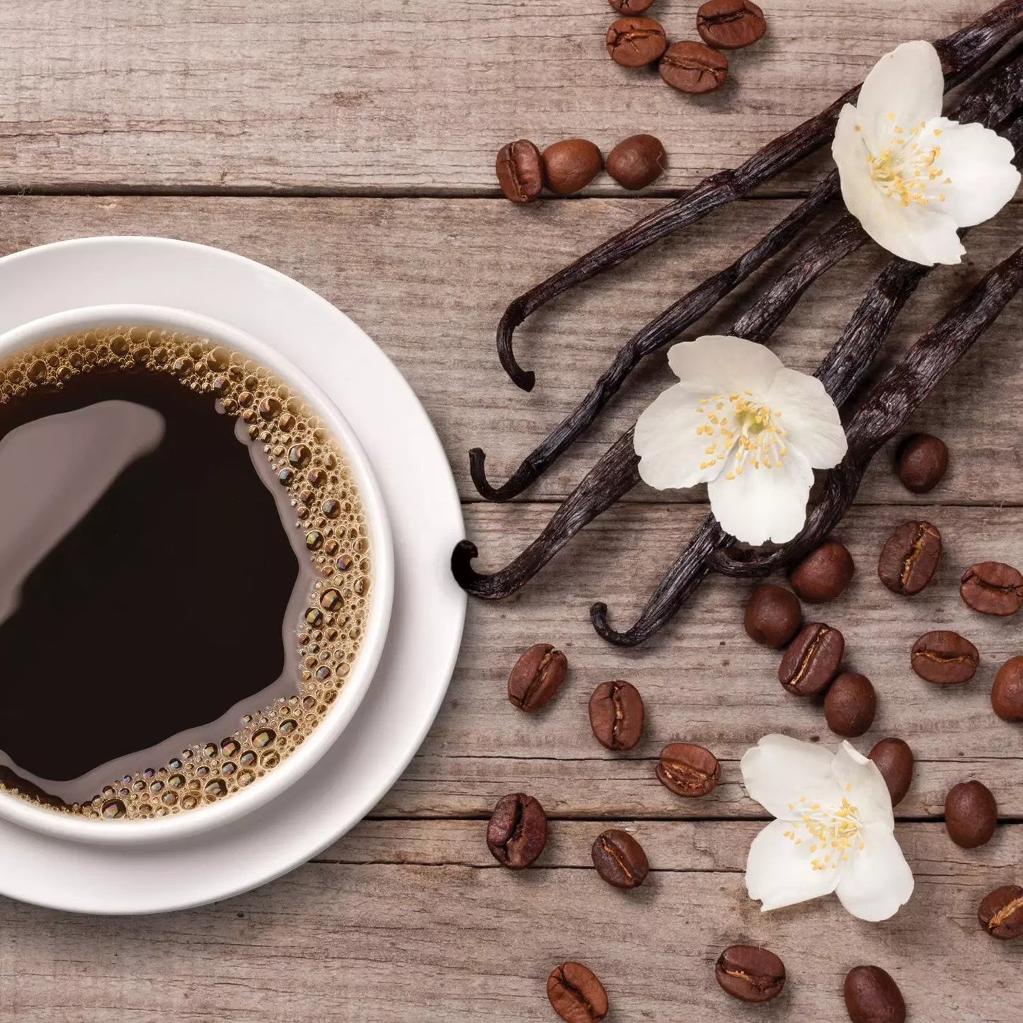 Cup of coffee with vanilla beans and flowers on a wooden surface