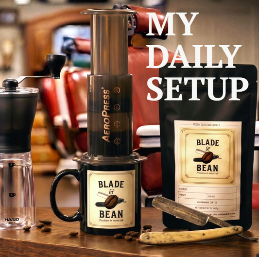A styled coffee setup on a wooden table featuring an AeroPress coffee maker, a black mug with a Blade & Bean label, a bag of Blade & Bean coffee, a manual grinder, a small glass carafe, and a spoon, with the text 'MY DAILY SETUP' overlaid on the image.