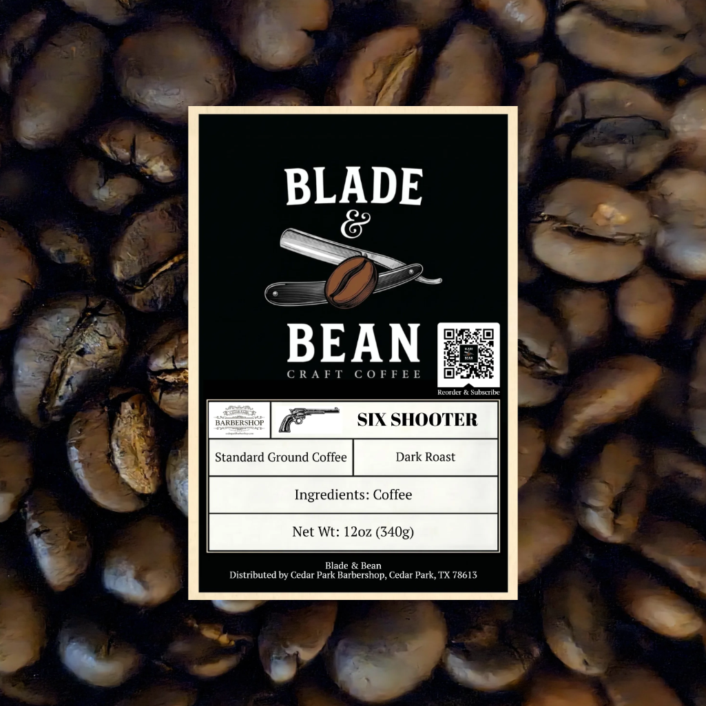 A rectangular coffee label for Blade & Bean Craft Coffee, shade Six Shooter, placed over a background of roasted coffee beans. The label is black with a cream border and white text, showing product details including roast, ground type, ingredients, and net weight.