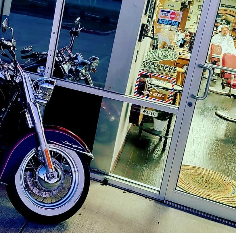 Motorcycle parked outside a barber shop with a reflection of the interior.