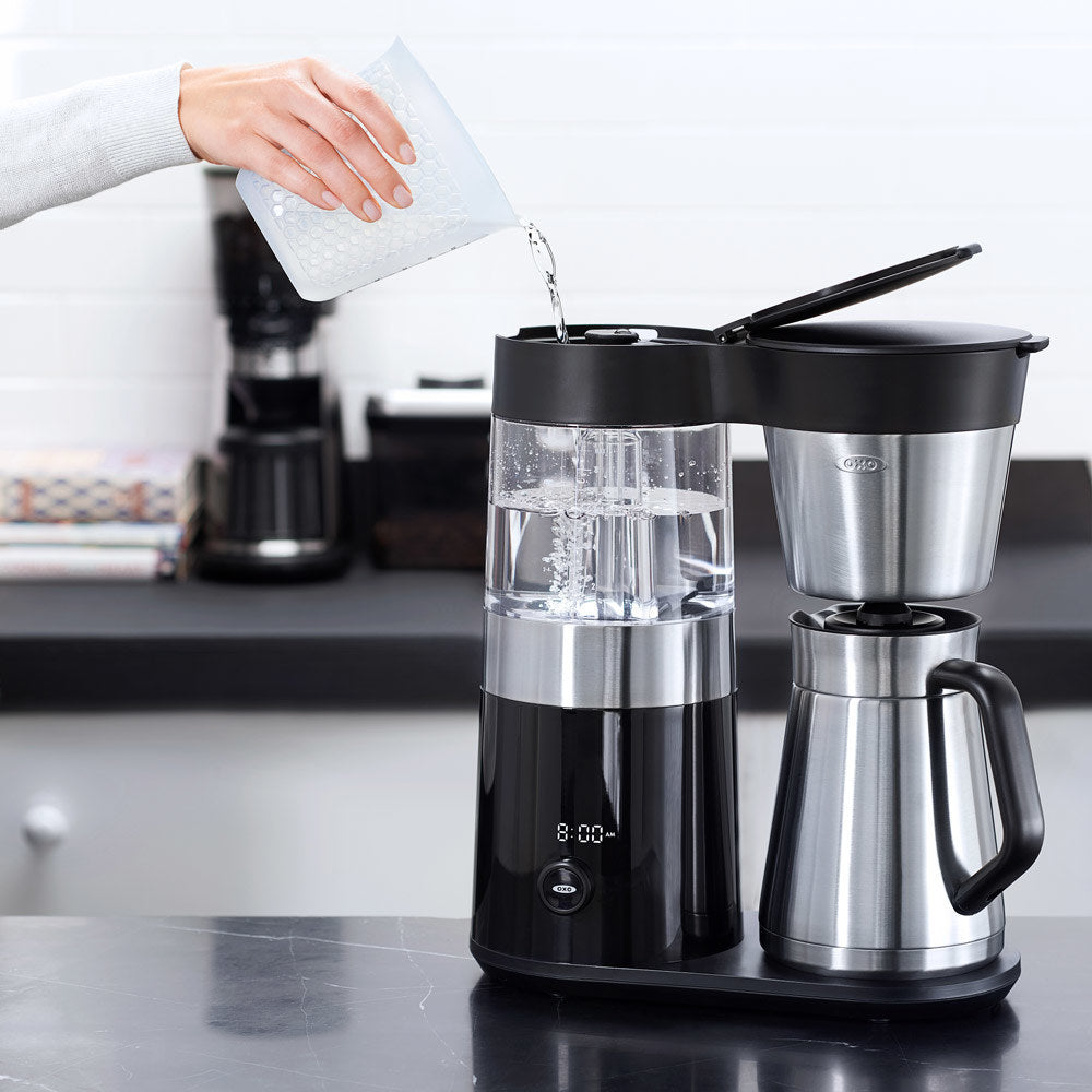 Person pouring water into a coffee maker on a kitchen counter.