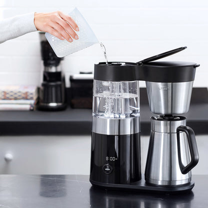 Person pouring water into a coffee maker on a kitchen counter.