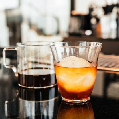 Two glasses of coffee and a cocktail on a desk with a blurred office background