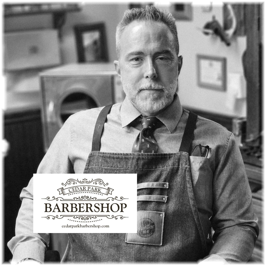 A black and white portrait of a man wearing a denim apron over a dress shirt and tie, standing in a barbershop environment. A white logo overlay at the bottom left reads 'CEDAR PARK BARBERSHOP' with 'cedarparkbarbershop.
