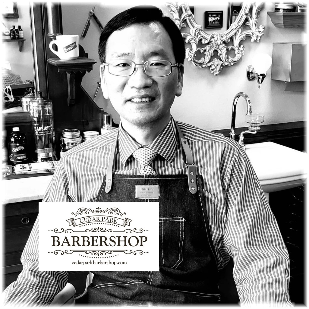 A black and white photo of a man wearing glasses, a striped shirt, tie, and dark apron in a barbershop setting. A white logo overlay at the bottom reads 'CEDAR PARK BARBERSHOP'.